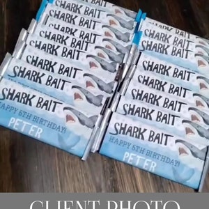 May include: A stack of chocolate bar wrappers featuring a shark graphic and the text "Shark Bait" printed on them. The wrappers are personalised with the text "Happy 6th Birthday Peter".
