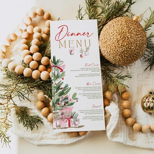 May include: A vertical dinner menu card featuring a watercolor illustration of a Christmas tree and gifts. The text reads Dinner MENU followed by First Course, Main Course, and Dessert sections with listed food items in red and black ink.