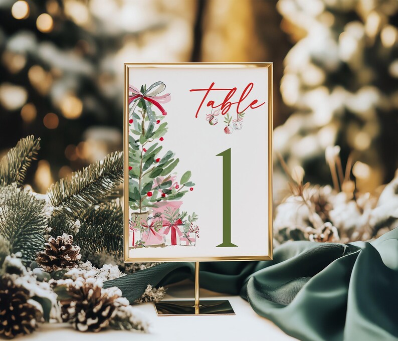 May include: A rectangular table number sign in a gold frame featuring a watercolor illustration of a Christmas tree with pink gifts and the red text Table 1 in a large green font. The design includes small hanging ornaments.