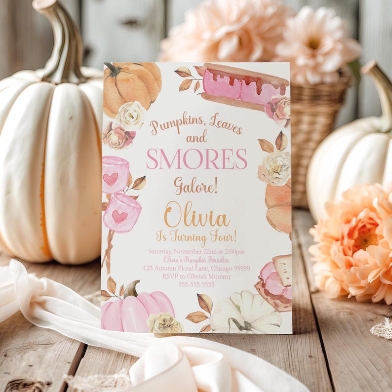 Printable Pumpkin and Smores Birthday Invitation styled on weathered wooden planks beside an oversized white pumpkin, peach garden blooms, woven baskets, and flowing ivory ribbon. The rustic farmhouse setting enhances the watercolor pumpkins, pink marshmallows, toasted smores, and soft floral artwork while showcasing this editable Canva invitation for a cozy autumn birthday party.