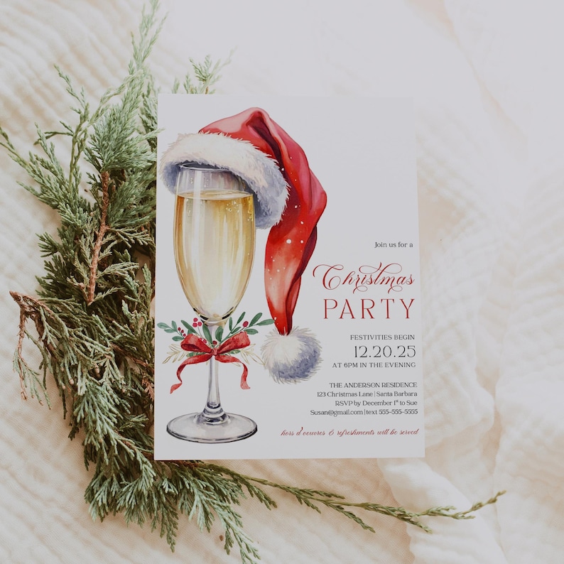 Christmas party invitation featuring a champagne glass with a Santa hat and red coquette bow, perfect for holiday cocktail parties or Friendsmas gatherings. The invitation has elegant red and black text that highlights the party details for an adult Christmas celebration. Shown flat on greenery and white fabric, the mockup creates a cozy winter feel that enhances the festive design.