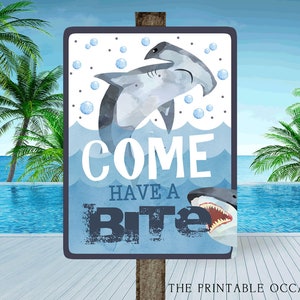 May include: A blue and white sign with a shark and hammerhead shark illustration. The sign says "Come Have a Bite".