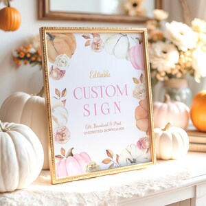 Editable fall pumpkin birthday sign with blush pink and ivory watercolor pumpkins, soft beige and rose florals, and golden fall leaves. Displayed in a gold frame on a white dresser with neutral fall props including lace fabric, mini pumpkins, and a dried floral arrangement. Text on the sign reads Editable Custom Sign in pink and brown serif fonts. Perfect for a girl’s fall birthday party or autumn-themed celebration.