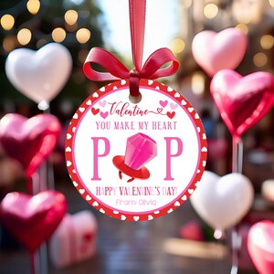 May include: A Valentine's Day ornament with a red ribbon. The round ornament has a white center with the words "You Make My Heart POP" and a graphic of a ring. The border is red with white hearts. The ornament says "Happy Valentine's Day!"