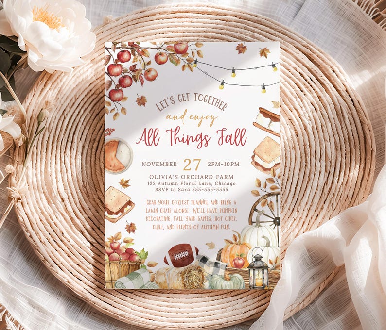 Autumn harvest party invitation with watercolor apples, s’mores, pumpkins and string lights framing the All Things Fall headline in warm rustic colors. Editable party details appear in the center with soft seasonal typography. The invitation sits on a woven placemat beside neutral florals and soft textured fabric adding an elegant farmhouse fall aesthetic.
