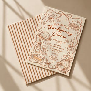 Hand drawn Thanksgiving dinner invitation shown with its coordinating striped backside on a warm cream surface. The design features brown line art with turkey, pie, pumpkins, wine, candles, bows and autumn leaves. Soft window shadows give the scene a warm Thanksgiving feel. Both the illustrated invitation front and matching striped reverse are visible.