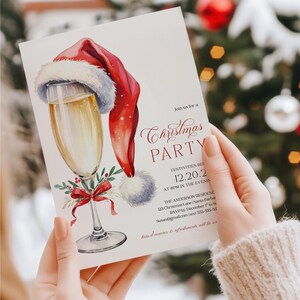 Editable Christmas invitation with a champagne glass topped with Santa hat and red bow, designed for festive cocktail parties and Friendsmas get-togethers. The template is perfect for holiday gatherings, office events, or adult Christmas celebrations. Shown outdoors with a blurred tree background, the mockup gives a natural, wintry vibe that complements the holiday theme.