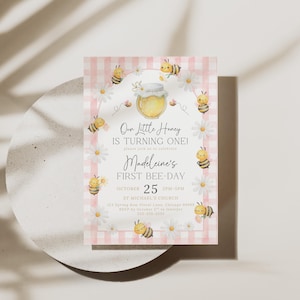 The Printable Occasions offers custom wedding birthday and baby shower templates for every celebration. Pink bee first birthday invitation featuring watercolor bees, daisies, honey jar, and pink gingham border. Shown on round ceramic plate with soft shadows. Editable Canva design perfect for a girl’s 1st bee day printable invitation.