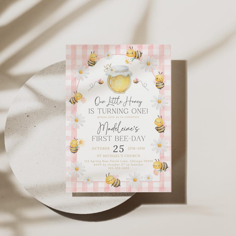 The Printable Occasions offers custom wedding birthday and baby shower templates for every celebration. Pink bee first birthday invitation featuring watercolor bees, daisies, honey jar, and pink gingham border. Shown on round ceramic plate with soft shadows. Editable Canva design perfect for a girl’s 1st bee day printable invitation.