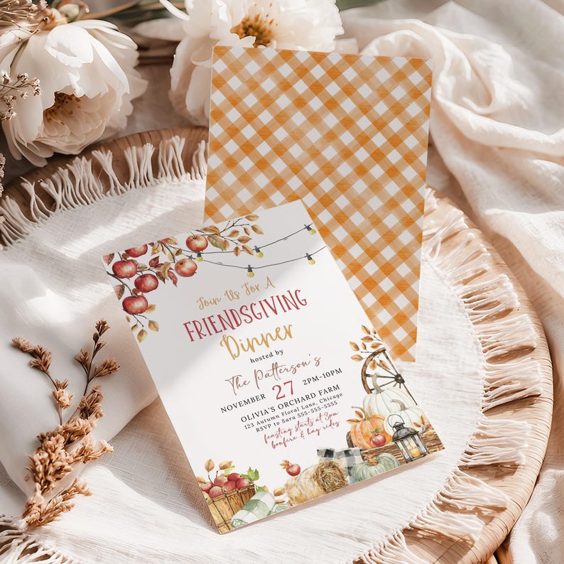 Elegant Rustic Fall Dinner Party invitation featuring watercolor apples, pumpkins and string lights arranged around the wording for a warm seasonal look. The invitation is displayed on a woven tray with white pumpkins, dried florals and flowing fabric that enhance the harvest inspired theme. Soft neutral styling gives the invitation a cozy autumn feel. This image highlights the printable Friendsgiving invitation design.