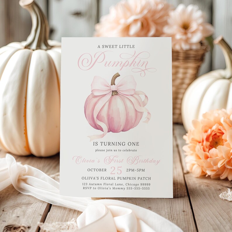 Editable girl’s pink pumpkin first birthday invitation placed among soft peachy florals and white pumpkins. The artwork features a large pink pumpkin with a flowing pastel bow and elegant fonts. Styled in a bright and airy flat lay with white drapery and wooden texture peeking through, this photo has a light coquette cottagecore vibe that blends baby girl charm with autumn elegance.