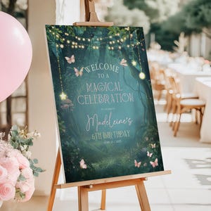 May include: A wooden easel displays a welcome sign for a magical celebration. The sign features a forest scene with butterflies, stars, and string lights. Text reads "Welcome to a Magical Celebration" and the name "Madeleine's" with the date.