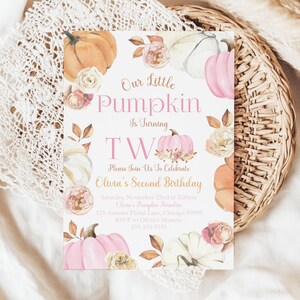Editable fall pumpkin second birthday invitation for girls from The Printable Occasion. Watercolor pumpkin artwork with blush roses and rustic foliage surrounds the text “Our Little Pumpkin is Turning Two.” The template is customizable in Canva. Mockup shows a set of invitations placed on soft neutral fabric with scattered pink dried flowers for a light autumn display.