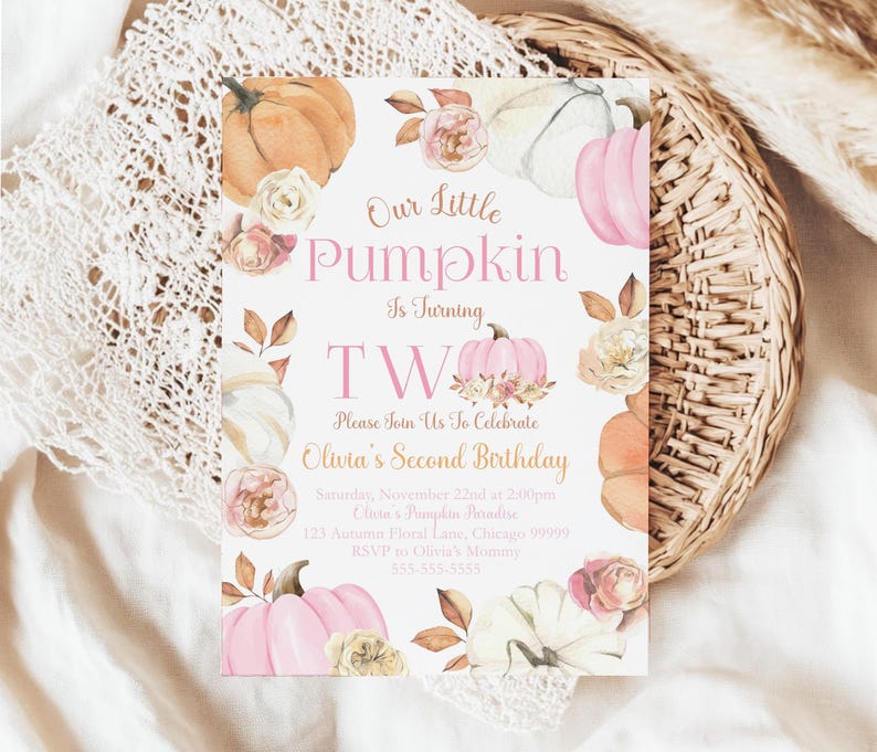 Editable fall pumpkin second birthday invitation for girls from The Printable Occasion. Watercolor pumpkin artwork with blush roses and rustic foliage surrounds the text “Our Little Pumpkin is Turning Two.” The template is customizable in Canva. Mockup shows a set of invitations placed on soft neutral fabric with scattered pink dried flowers for a light autumn display.