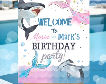May include: A party sign on a wooden easel with a mermaid and shark theme. The sign reads "WELCOME to Maria and Mark's BIRTHDAY party!" in blue, pink, and gray lettering. Watercolor illustrations of sharks and mermaid tails decorate the sign.