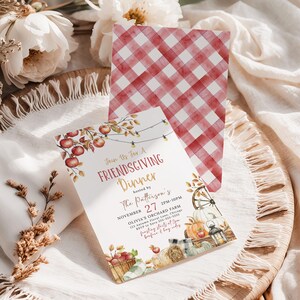 Charming Friendsgiving Dinner invitation displayed with the optional red gingham backside and watercolor autumn artwork on the front. The design features apples, pumpkins, lanterns and harvest elements that perfectly capture a cozy Thanksgiving gathering. The stationery rests on layered cream fabrics with soft florals and dried stems surrounding the cards. This image showcases one of the included backside color options.