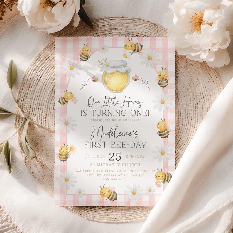 The Printable Occasions offers custom wedding birthday and baby shower templates for every celebration. Editable pink bee birthday invitation with watercolor bumblebees holding flowers, daisies, honey jar, and pink gingham border. Displayed on woven placemat with white fabric and peonies. Canva template for a girl’s first bee day party with printable download.