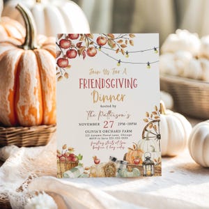 Inviting Friendsgiving Dinner invitation featuring watercolor apples, pumpkins and harvest details displayed among pumpkins and soft neutral linens. The printable invitation is styled with warm lighting that creates a cozy autumn atmosphere perfect for a Thanksgiving gathering. Rustic seasonal elements frame the design without distracting from the invitation wording. This image highlights the elegant fall party invitation.