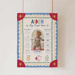 May include: A rectangular milestone poster titled Aiden My First Year with a central photo of a baby. The design features red, blue, and green borders with stars. Text includes personality, favorite foods, songs, books, toys, 35 lbs, 6 teeth, and 32 inches.