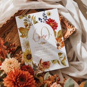 May include: A rectangular invitation card featuring a white background with watercolor floral illustrations in shades of red, orange, yellow, and blue. The text reads 60 sixty, Please join us to celebrate, Olivia St James, Saturday, November 25th 2026.