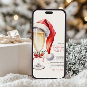 Digital Christmas party evite with champagne glass, Santa hat, and coquette bow, designed for instant download and easy holiday party planning. The template is mobile-friendly, so guests can receive and view details instantly on their phone for any holiday cocktail or Friendsmas event. Mockup styling with a wrapped gift and snowy backdrop highlights the convenience of sending a stylish Christmas invitation digitally.