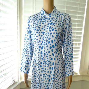 May include: A long-sleeved dress with a white base and a pattern of blue spots. The dress features a collared neckline and buttons down the front. The dress is knee-length, approximately 100 cm.