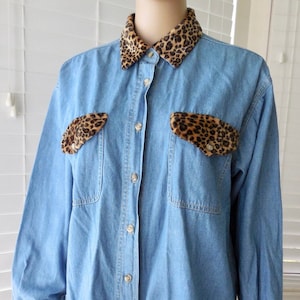 May include: A light blue denim shirt with leopard print trim on the collar, pockets, and cuffs.