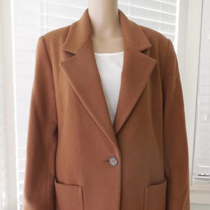 May include: A brown blazer with a single button closure and two front pockets. The blazer is displayed on a mannequin, paired with a white top and blue jeans. The blazer's color is a warm, earthy tone.