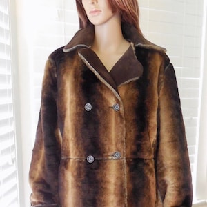 May include: A brown and tan faux fur coat with a double-breasted closure and brown suede trim. The coat has a collar and long sleeves.