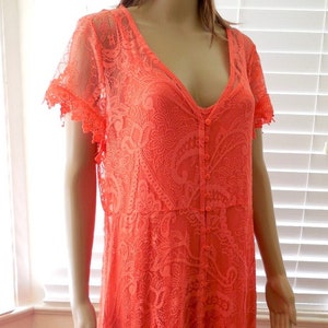May include: A coral-colored lace maxi dress with a V-neckline and button-up front. The dress has short sleeves with lace trim and a flowing skirt.