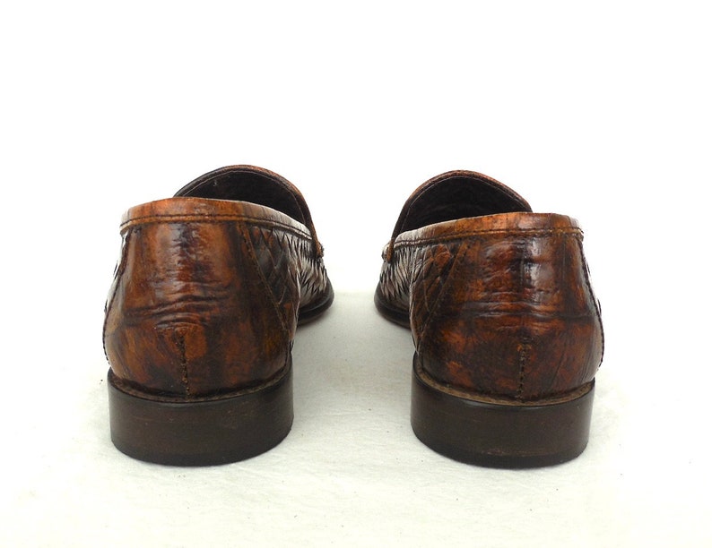 May include: A pair of brown leather loafers with a woven pattern. The loafers have a dark brown sole and a slightly pointed toe.