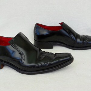 Puede incluir: Un par de zapatos negros de cuero con un dise&ntilde;o de punta y detalles de brogue. Los zapatos tienen un forro de cuero rojo.