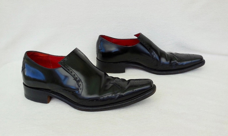 Puede incluir: Un par de zapatos negros de cuero con un dise&ntilde;o de punta y detalles de brogue. Los zapatos tienen un forro de cuero rojo.