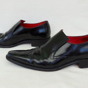 Puede incluir: Un par de zapatos negros de cuero con cordones, punta puntiaguda y detalles de brogue. Los zapatos tienen un forro de cuero rojo.