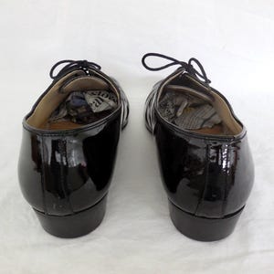 Puede incluir: Par de zapatos de vestir negros de charol con cordones. Los zapatos tienen un acabado brillante y est&aacute;n vac&iacute;os, con papel en el interior. Los zapatos est&aacute;n sobre una superficie blanca.