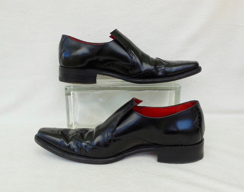 Puede incluir: Un par de zapatos negros de cuero con un dise&ntilde;o de punta y detalles de brogue. Los zapatos tienen un forro de cuero rojo.
