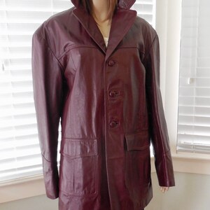 May include: A burgundy leather jacket with a button-up front and two large pockets. The jacket has a classic style and is made of high-quality leather.