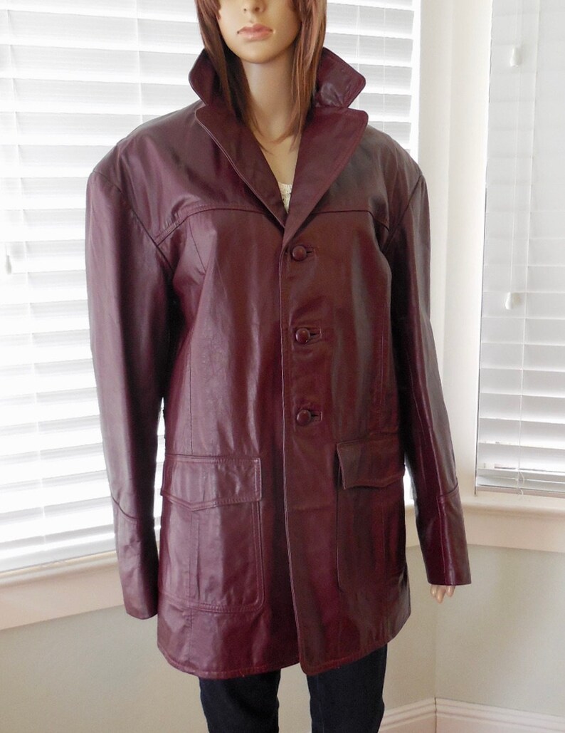 May include: A burgundy leather jacket with a button-up front and two large pockets. The jacket has a classic style and is made of high-quality leather.