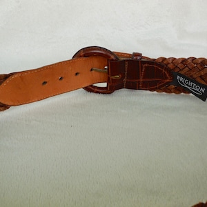 May include: A brown leather braided belt with a silver buckle and a Brighton brand label.