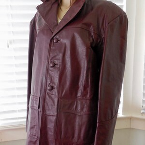 May include: A burgundy leather jacket with a button-up front and two pockets. The jacket has a collar and long sleeves.