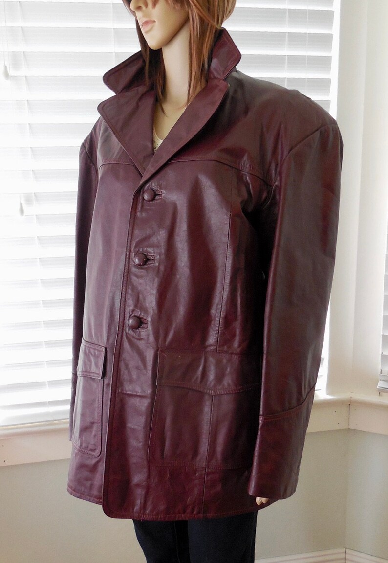 May include: A burgundy leather jacket with a button-up front and two pockets. The jacket has a collar and long sleeves.