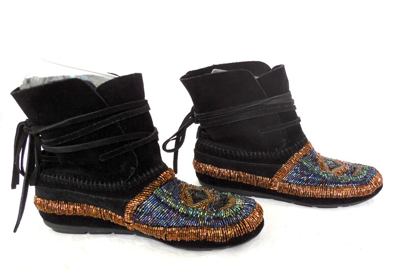 K&ouml;nnte beinhalten: Paar schwarze Wildleder-Ankle Boots mit Perlenbesatz. Die Stiefel haben einen Wickelverschluss und sind mit aufwendigen Perlenarbeiten in Blau, Gr&uuml;n und Kupfer verziert. Die Sohlen sind schwarz.