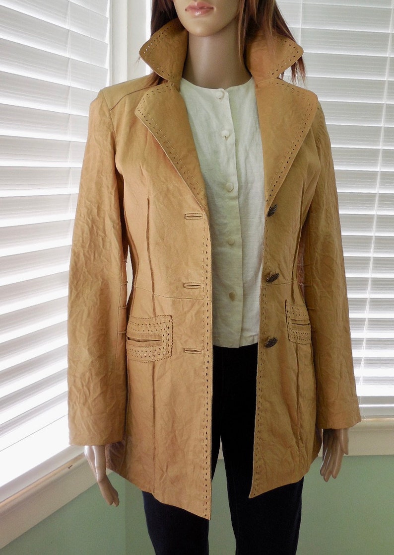 May include: A tan leather jacket with decorative stitching and button closures. The jacket has a long, fitted silhouette.