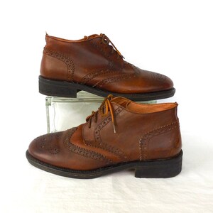 Pode incluir: Um par de sapatos de couro marrom brogue com fecho de cadar&ccedil;o. Os sapatos t&ecirc;m um design de ponta de asa e uma sola texturizada.