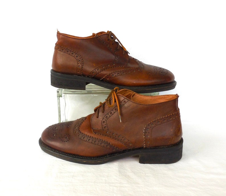 Pode incluir: Um par de sapatos de couro marrom brogue com fecho de cadar&ccedil;o. Os sapatos t&ecirc;m um design de ponta de asa e uma sola texturizada.
