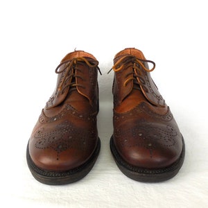Pode incluir: Um par de sapatos de couro marrom com design de ponta de asa e fecho de cadar&ccedil;o.