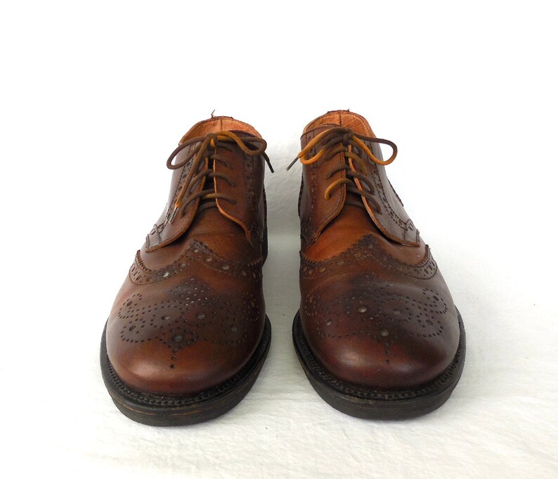 Pode incluir: Um par de sapatos de couro marrom com design de ponta de asa e fecho de cadar&ccedil;o.