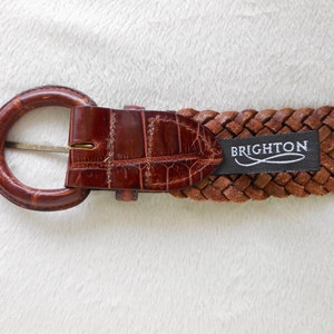 May include: A brown leather braided belt with a brown crocodile embossed buckle and a black label that reads "BRIGHTON".