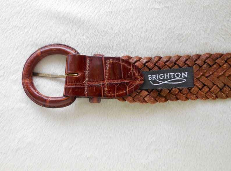 May include: A brown leather braided belt with a brown crocodile embossed buckle and a black label that reads "BRIGHTON".