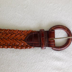 May include: A brown leather belt with a braided design and a round buckle.